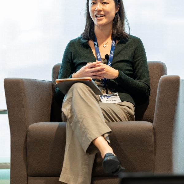 Alice Hau speaking on stage with legs crossed, sitting in a chair.